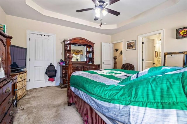 bedroom with ceiling fan, light colored carpet, and a tray ceiling