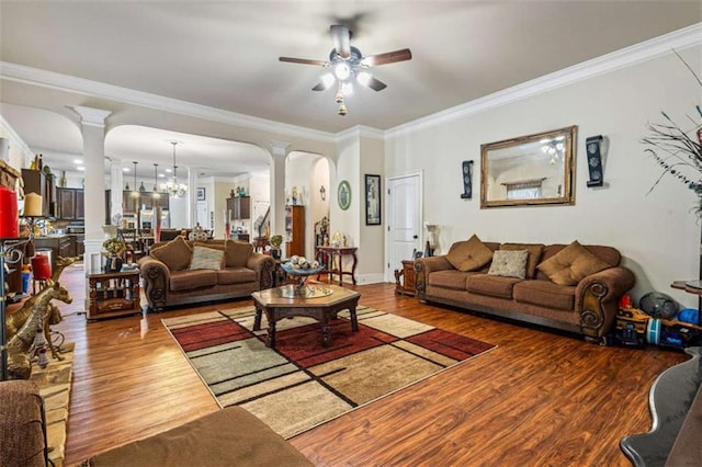 living room with ornate columns, wood-type flooring, ceiling fan with notable chandelier, and crown molding