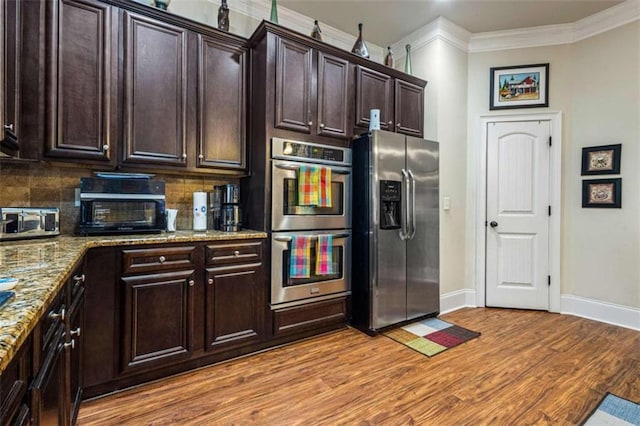 kitchen with stainless steel appliances, crown molding, light stone countertops, and dark brown cabinetry