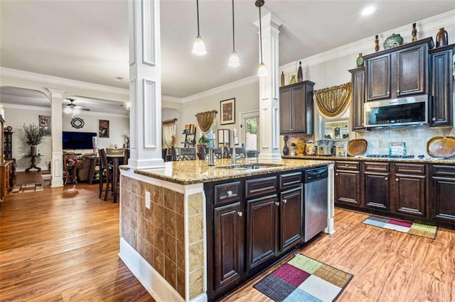 kitchen with ornate columns, an island with sink, sink, stainless steel appliances, and dark brown cabinets