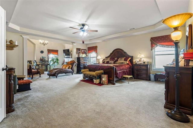 carpeted bedroom with a tray ceiling and ceiling fan with notable chandelier