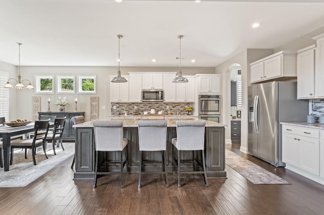 kitchen with appliances with stainless steel finishes, white cabinetry, tasteful backsplash, arched walkways, and a kitchen island