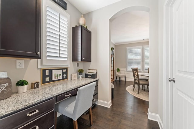 office space featuring arched walkways, dark wood-style flooring, built in study area, and baseboards