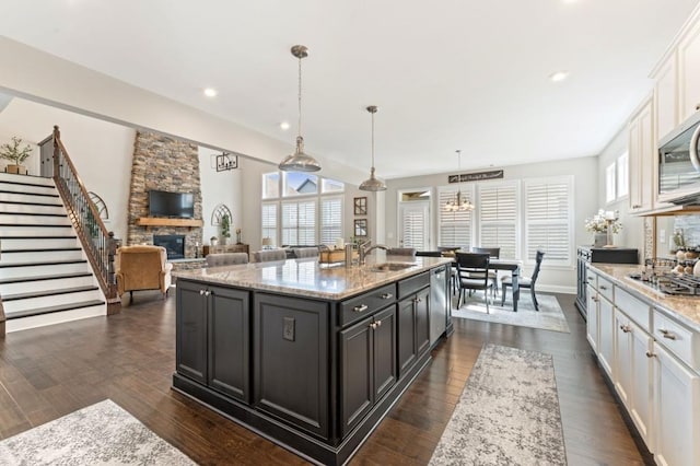 kitchen with white cabinets, a sink, a fireplace, stainless steel appliances, and dark wood-type flooring