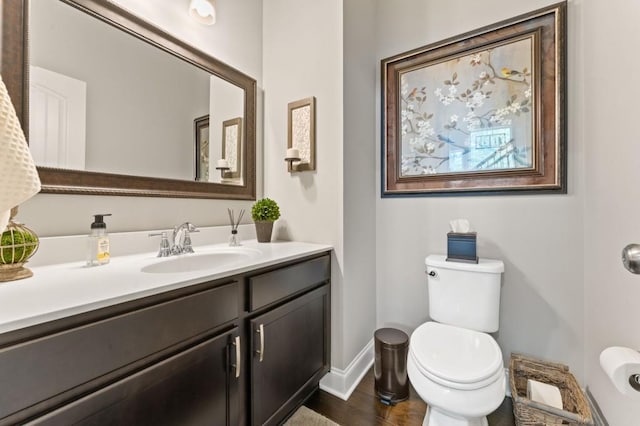 half bathroom with baseboards, toilet, vanity, and wood finished floors