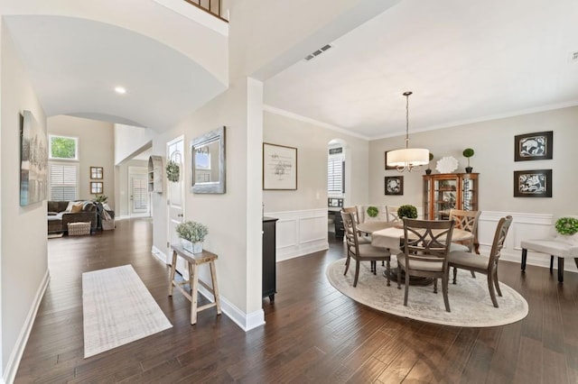 dining space with arched walkways, plenty of natural light, dark wood-style floors, a wainscoted wall, and crown molding