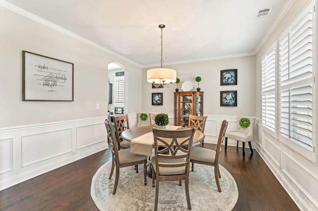 dining space featuring dark wood finished floors, a chandelier, crown molding, arched walkways, and a wainscoted wall