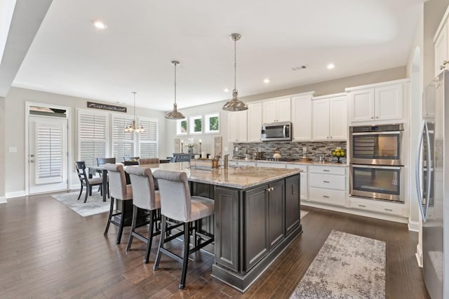 kitchen featuring stainless steel appliances, white cabinets, backsplash, a kitchen island with sink, and dark wood-type flooring