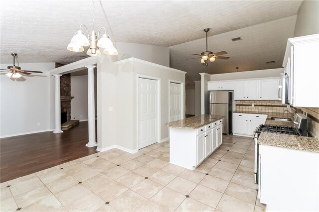 kitchen with light stone counters, stainless steel appliances, a center island, white cabinetry, and hanging light fixtures