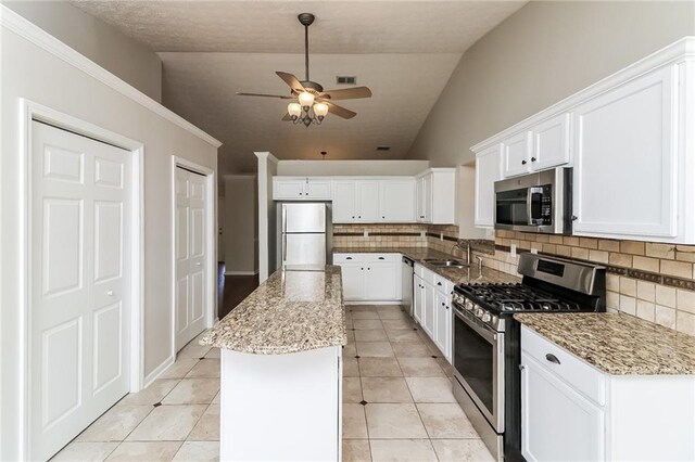 kitchen with white cabinets, a kitchen island, appliances with stainless steel finishes, and vaulted ceiling