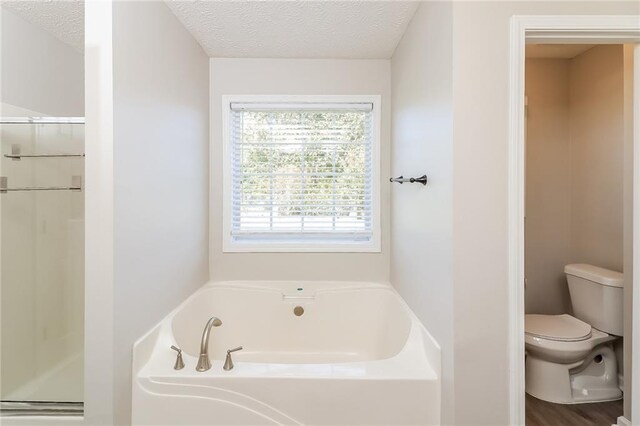 bathroom featuring hardwood / wood-style flooring, shower with separate bathtub, toilet, and a textured ceiling