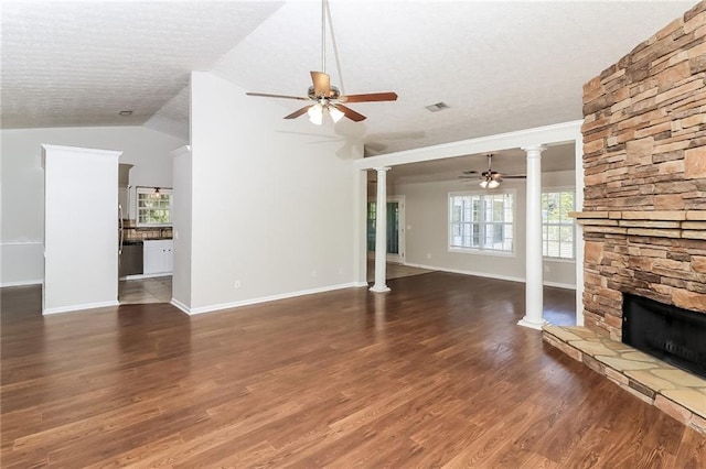 unfurnished living room with vaulted ceiling, a stone fireplace, ornate columns, and dark hardwood / wood-style floors