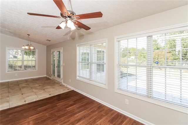 empty room featuring lofted ceiling, plenty of natural light, wood-type flooring, and a textured ceiling