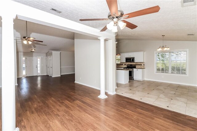 unfurnished living room featuring ceiling fan with notable chandelier, vaulted ceiling, hardwood / wood-style flooring, ornate columns, and a textured ceiling