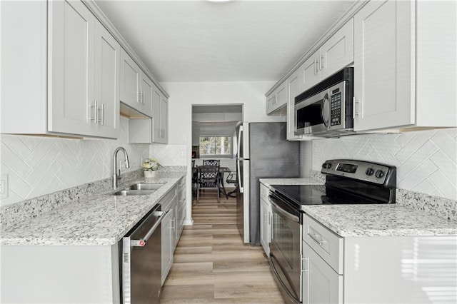 kitchen with sink, decorative backsplash, light hardwood / wood-style floors, light stone counters, and stainless steel appliances