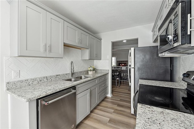 kitchen with gray cabinetry, sink, light hardwood / wood-style floors, light stone counters, and stainless steel appliances