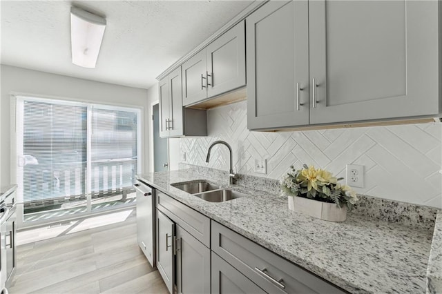 kitchen with sink, stainless steel dishwasher, decorative backsplash, gray cabinets, and light stone counters