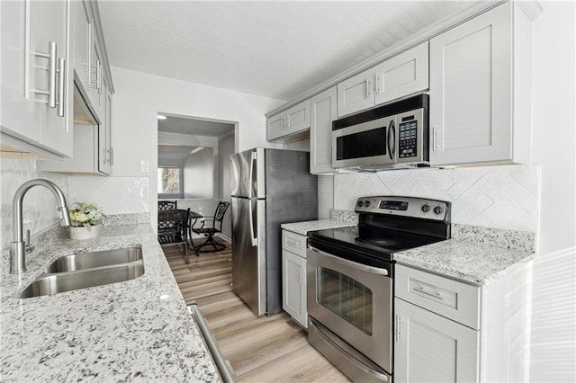 kitchen featuring decorative backsplash, appliances with stainless steel finishes, light wood-type flooring, light stone counters, and sink