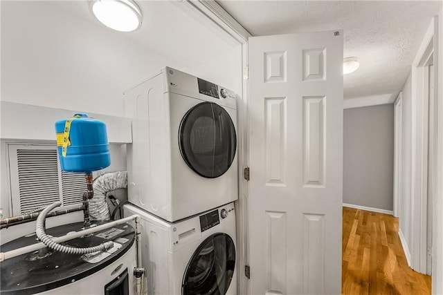 washroom featuring baseboards, stacked washer / dryer, light wood-style flooring, a textured ceiling, and water heater