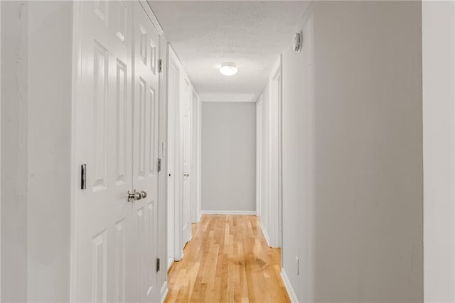 hall with light wood-type flooring, a textured ceiling, and baseboards