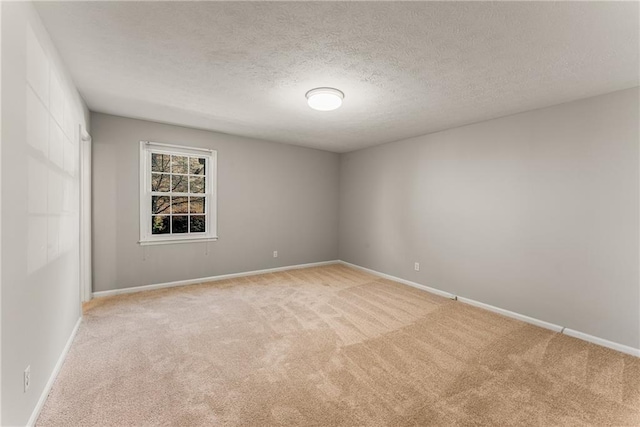 spare room with light colored carpet, a textured ceiling, and baseboards