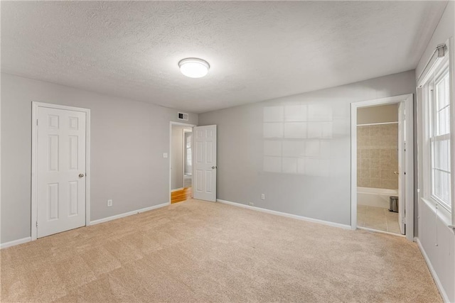 unfurnished bedroom featuring a textured ceiling, ensuite bathroom, carpet flooring, visible vents, and baseboards