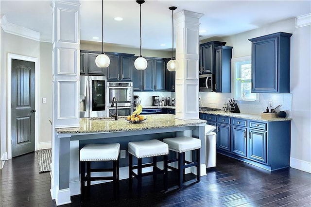 kitchen featuring tasteful backsplash, decorative light fixtures, an island with sink, stainless steel appliances, and light stone countertops