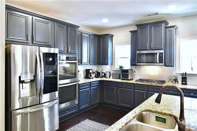 kitchen with appliances with stainless steel finishes, dark hardwood / wood-style floors, tasteful backsplash, sink, and light stone counters