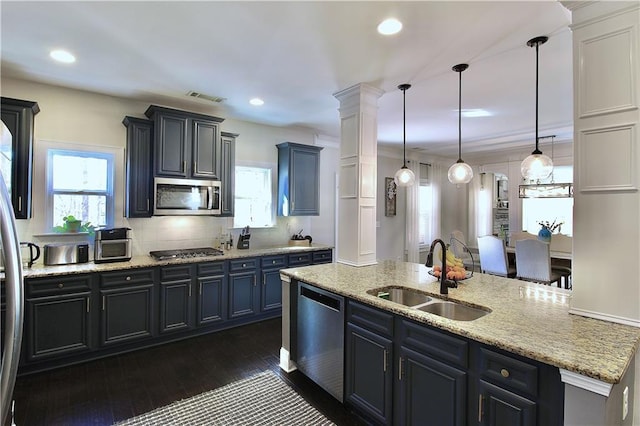 kitchen featuring sink, appliances with stainless steel finishes, hanging light fixtures, dark hardwood / wood-style floors, and an island with sink