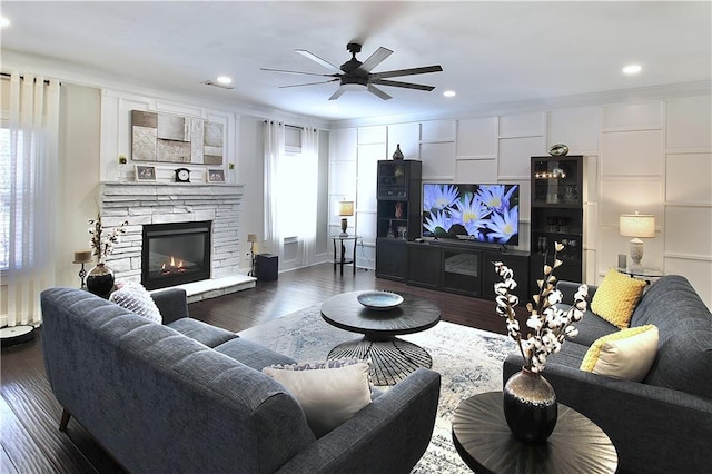 living room with a stone fireplace, ornamental molding, dark hardwood / wood-style floors, and ceiling fan