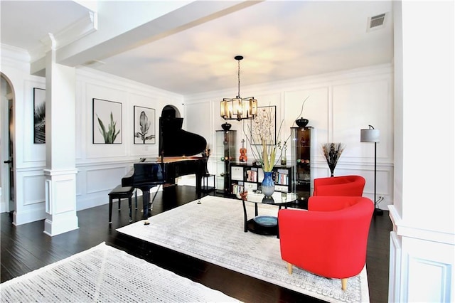 living room featuring an inviting chandelier, dark hardwood / wood-style flooring, ornamental molding, and ornate columns