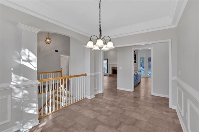 corridor with an inviting chandelier, crown molding, stone finish floor, arched walkways, and an upstairs landing
