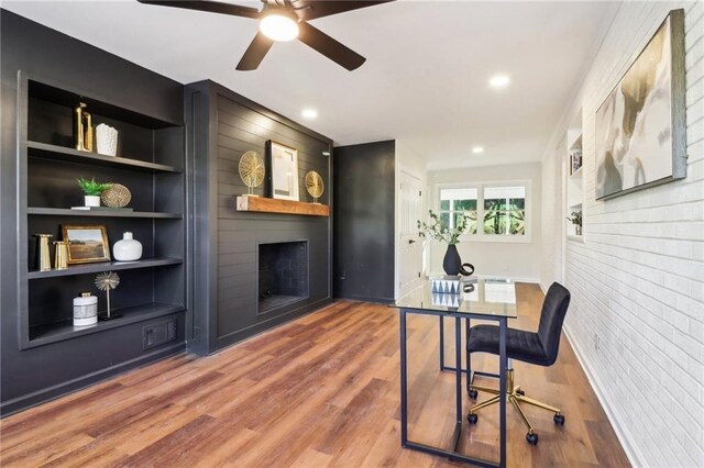 office space featuring ceiling fan, built in features, a large fireplace, and hardwood / wood-style flooring