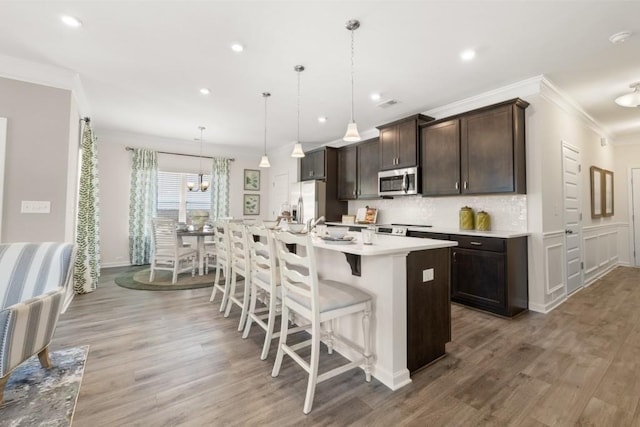 kitchen with a kitchen breakfast bar, light hardwood / wood-style flooring, an island with sink, pendant lighting, and appliances with stainless steel finishes