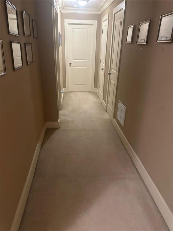 hall featuring crown molding, baseboards, light carpet, and visible vents
