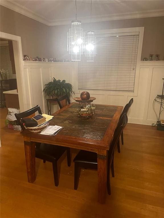 dining room with wood finished floors, a notable chandelier, ornamental molding, and a decorative wall