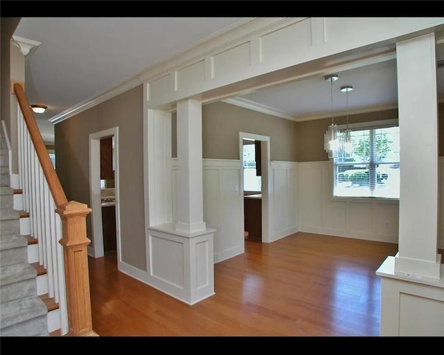 unfurnished dining area with light wood-style flooring, crown molding, a wainscoted wall, and stairs