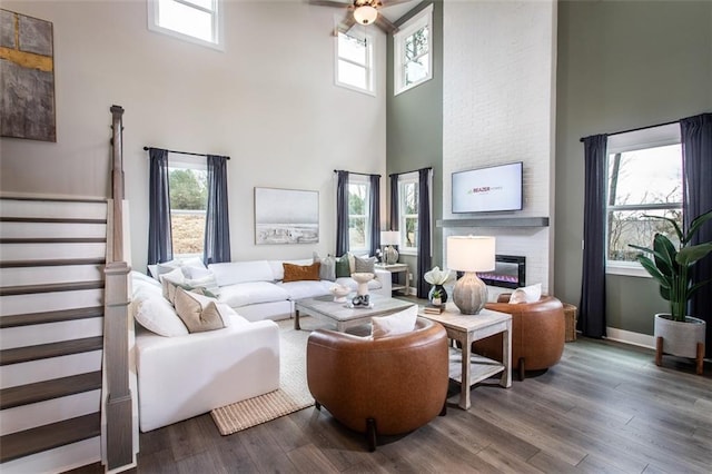 living room with wood-type flooring, ceiling fan, a large fireplace, and a towering ceiling