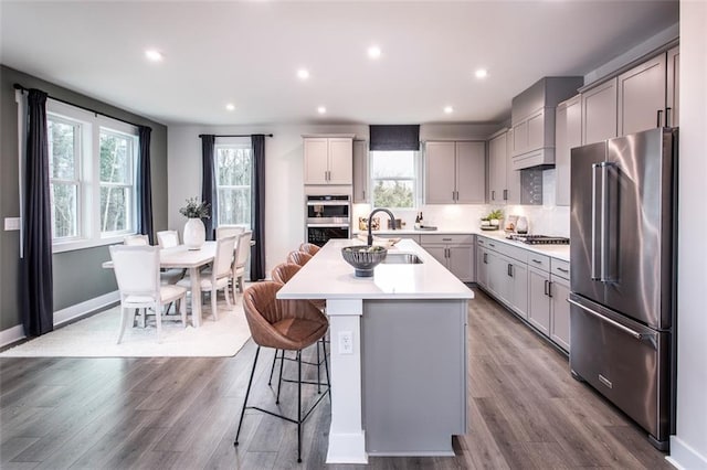 kitchen with appliances with stainless steel finishes, gray cabinetry, a kitchen breakfast bar, sink, and an island with sink