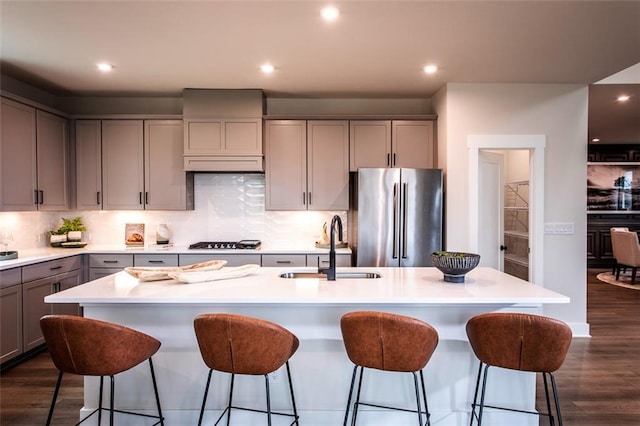 kitchen with sink, an island with sink, stainless steel refrigerator, and gray cabinetry