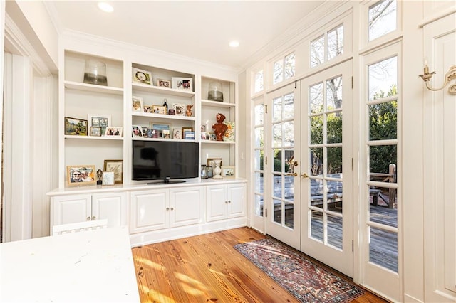 interior space featuring built in shelves, recessed lighting, ornamental molding, light wood-style floors, and french doors