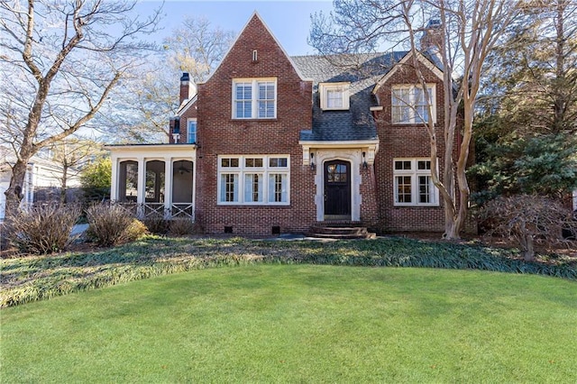 view of front facade featuring brick siding, roof with shingles, a chimney, and a front lawn