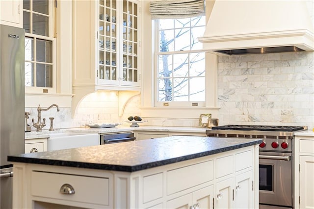 kitchen with backsplash, appliances with stainless steel finishes, custom range hood, and a sink