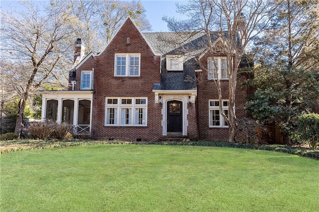 view of front facade featuring brick siding, a chimney, a front yard, and a sunroom