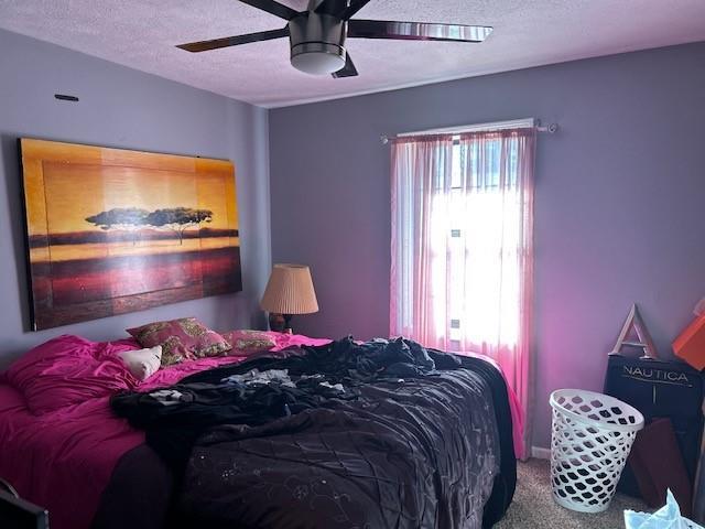 bedroom with ceiling fan, carpet flooring, and a textured ceiling