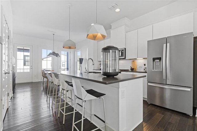 kitchen with a center island with sink, white cabinets, stainless steel appliances, and decorative light fixtures