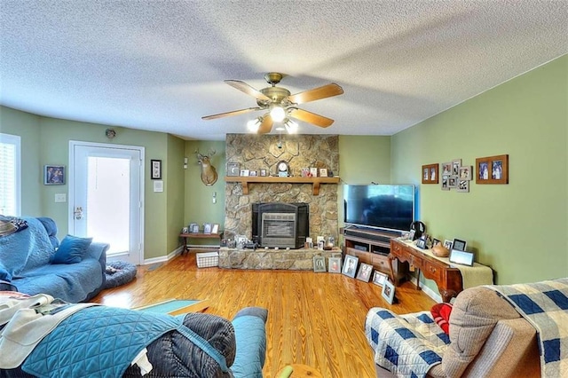 living room with a stone fireplace, a wealth of natural light, wood-type flooring, and ceiling fan