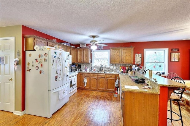 kitchen with a breakfast bar area, ceiling fan, white appliances, and light wood-type flooring