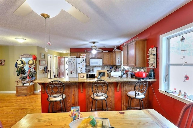 kitchen featuring ceiling fan, light hardwood / wood-style floors, kitchen peninsula, and white appliances