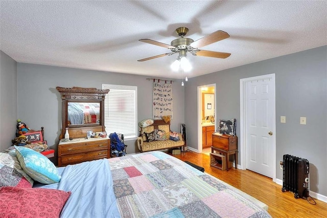 bedroom featuring light hardwood / wood-style floors, ensuite bathroom, ceiling fan, radiator heating unit, and a textured ceiling